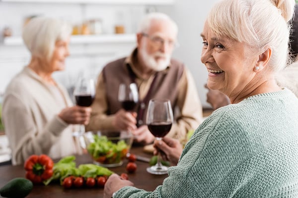 happy-senior-woman-holding-glass-red-wine-retired-friends-blurred-1